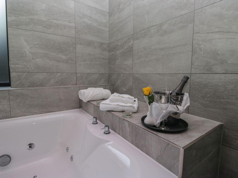 A bathroom with bathtub, towels, champagne and a flower at Lilac Cottage in Grange-Over-Sands