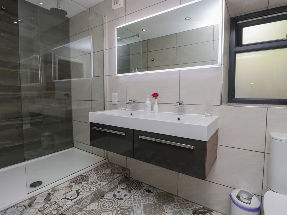 A bathroom with a sink, toilet, shower, and mirror at Lilac Cottage in Grange-Over-Sands