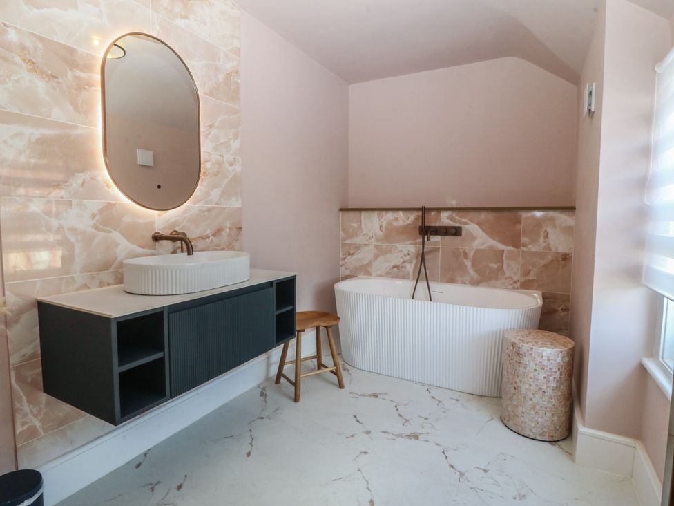A bathroom featuring a sink, mirror, bathtub and stool at Fox House in Llandudno