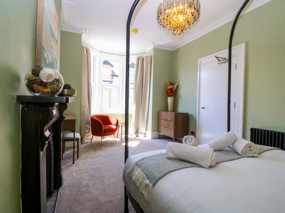 A bedroom with a bed, chair, cabinet and window at Fox House in Llandudno