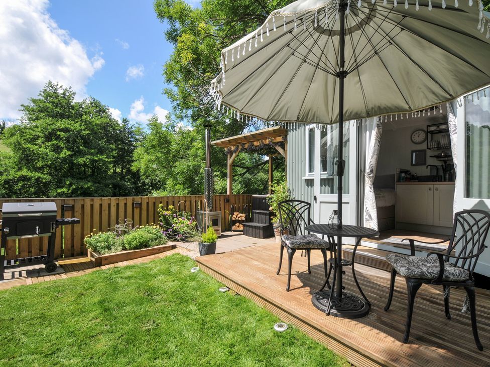 An outdoor space with a table and chairs under an umbrella at The Highwood Hut near Liskeard