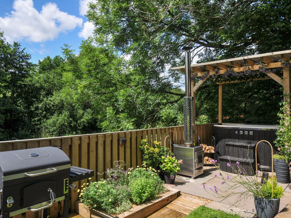 An outdoor deck with a grill and hot tub at The Highwood Hut near Liskeard