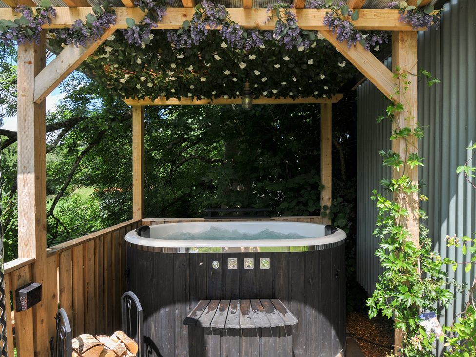 An outdoor hot tub surrounded by wood and plants at The Highwood Hut near Liskeard