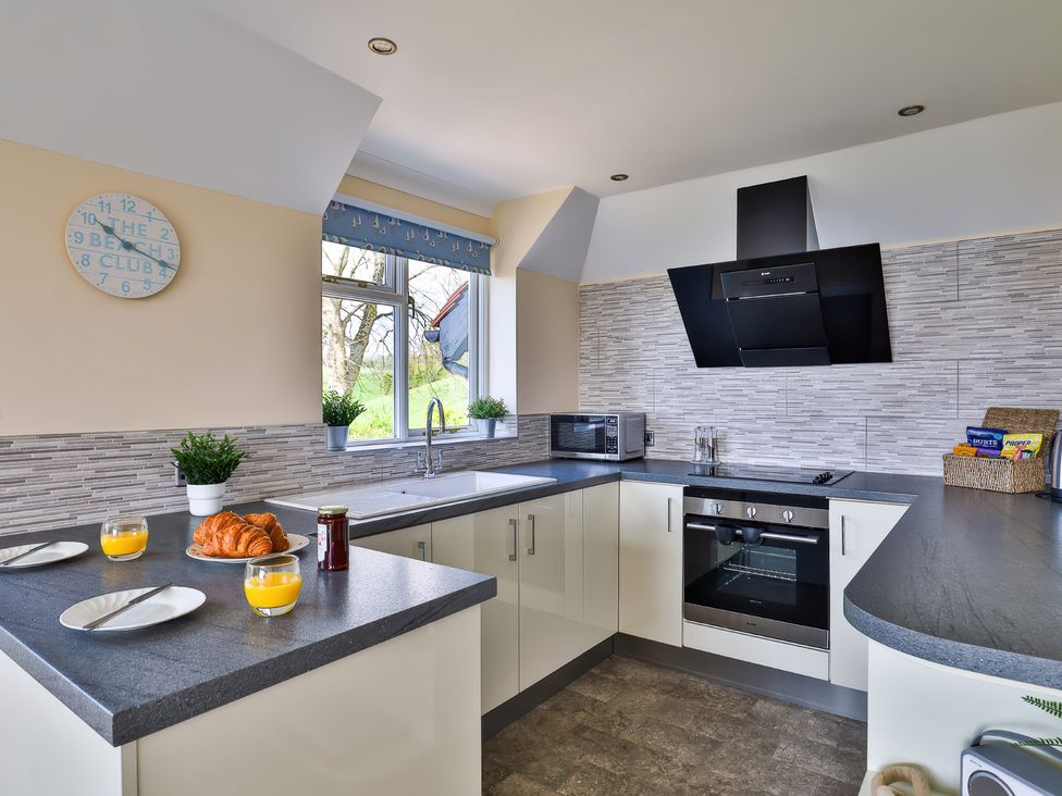 A kitchen with a countertop holding plates with croissants orange juice and jam near a window with potted plants at Beer View Cottage in Beer