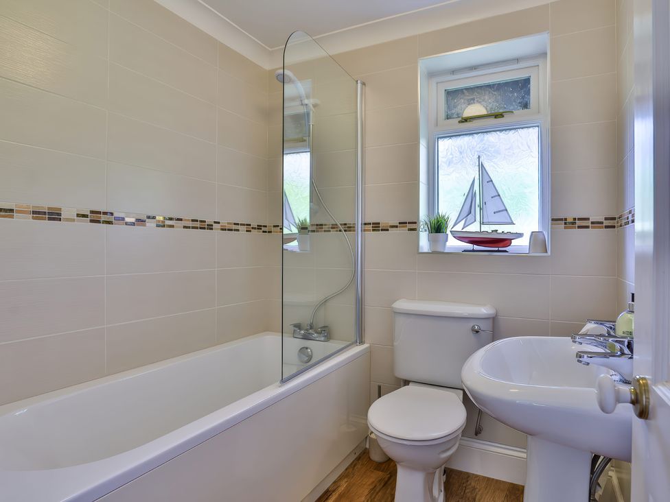 A bathroom with bathtub shower toilet sink and window with decorative sailboat at Beer View Cottage in Beer