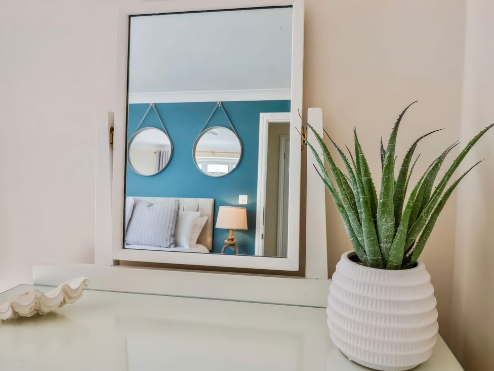 A mirror on a wall reflecting a bed with pillows two round mirrors and a lamp next to a white pot with a green plant at Beer View Cottage in Beer
