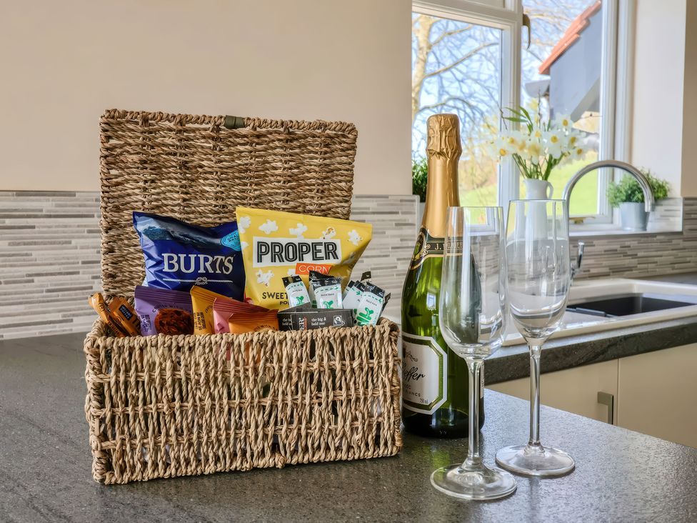 A kitchen counter with a wicker basket of snacks a bottle of champagne and two empty glasses at Beer View Cottage in Beer