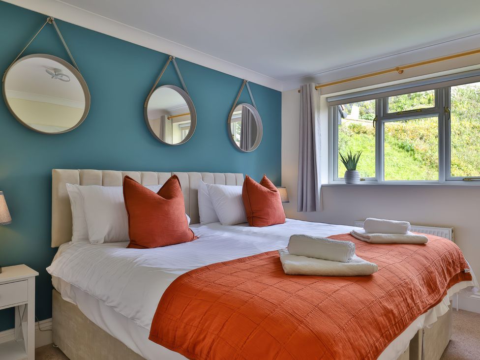 A bedroom with a bed with orange pillows and blanket three round mirrors on a blue wall and a window with a plant on the sill at Beer View Cottage in Beer