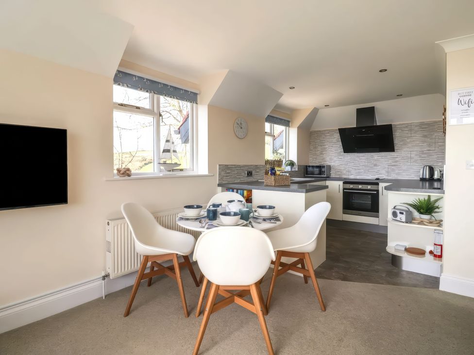 A kitchen and dining area with a round table set for four and a television on the wall at Beer View Cottage in Beer
