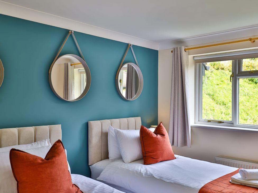 A bedroom with two single beds orange pillows round mirrors and a window at Beer View Cottage in Beer