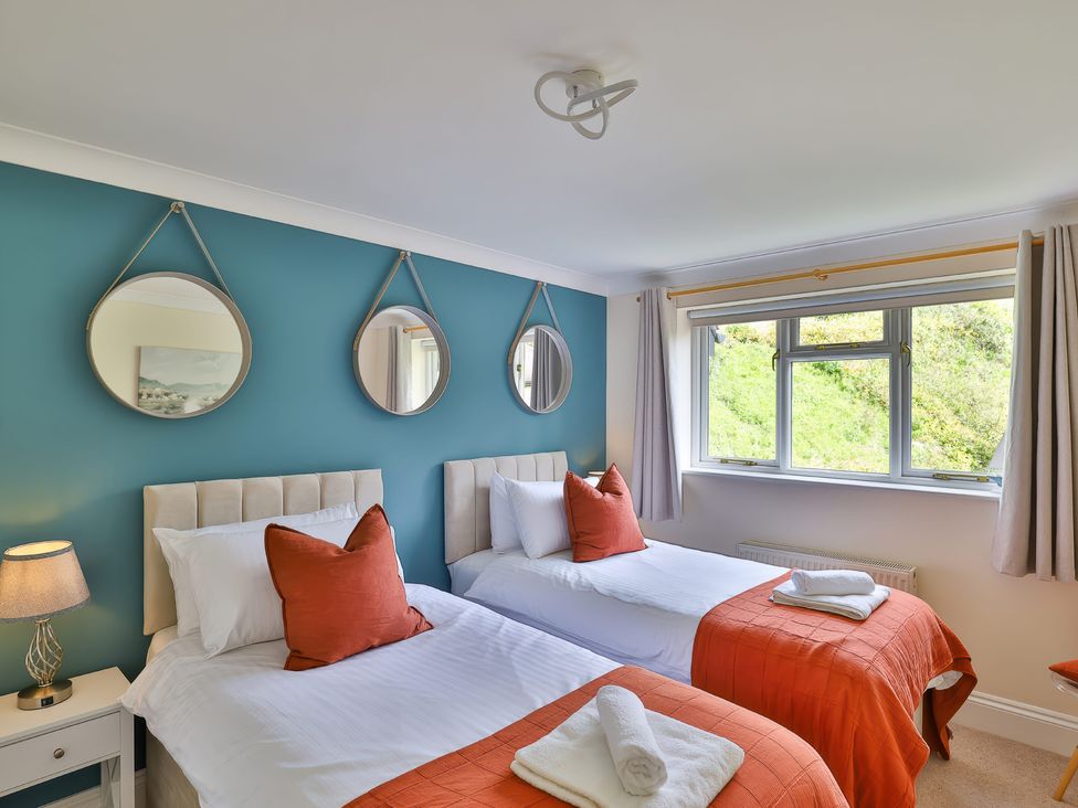 A bedroom with two single beds with orange throws and pillows and three round mirrors on a blue wall at Beer View Cottage in Beer