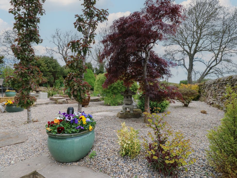 A garden with gravel pathways various trees potted flowers and a stone lantern at Pagecroft Cottage in Haydon Bridge
