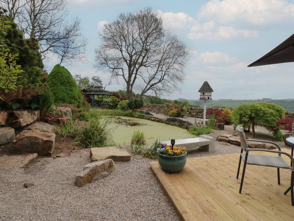 A garden with a pond a stone bench plants a birdhouse and outdoor chairs at Pagecroft Cottage in Haydon Bridge