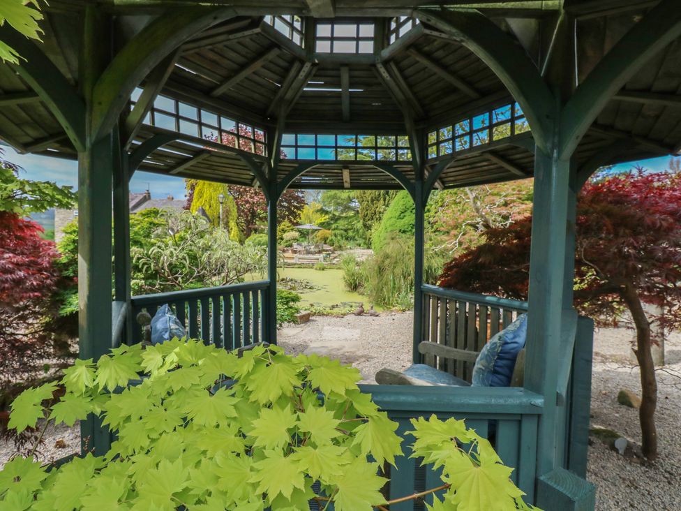 A wooden gazebo with blue cushions surrounded by greenery and a garden view at Pagecroft Cottage in Haydon Bridge