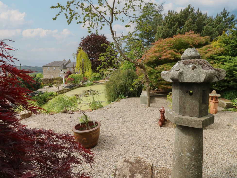 A garden with gravel paths a pond a stone lantern various trees and shrubs at Pagecroft Cottage in Haydon Bridge