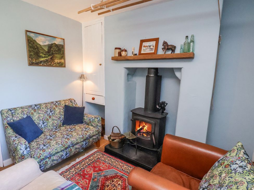 A sitting room with a wood burning stove two sofas a painting on the wall and a rug on the floor at Whinstone Cottage in Esk Valley near Grosmont