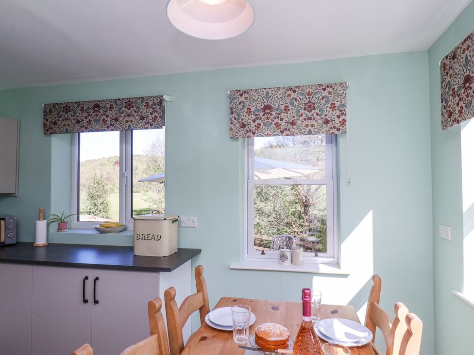 A kitchen with floral window blinds a wooden dining table set with plate a cake and a bottle at Whinstone Cottage Esk Valley near Grosmont