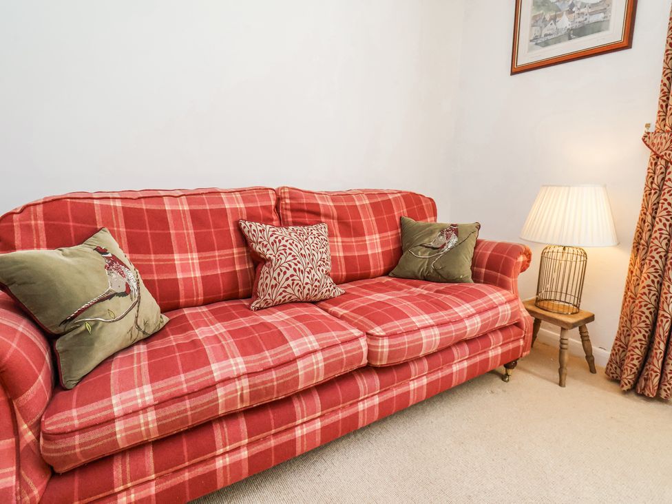 A red plaid sofa with decorative pillows beside a small wooden table with a lamp at Whinstone Cottage in Esk Valley near Grosmont