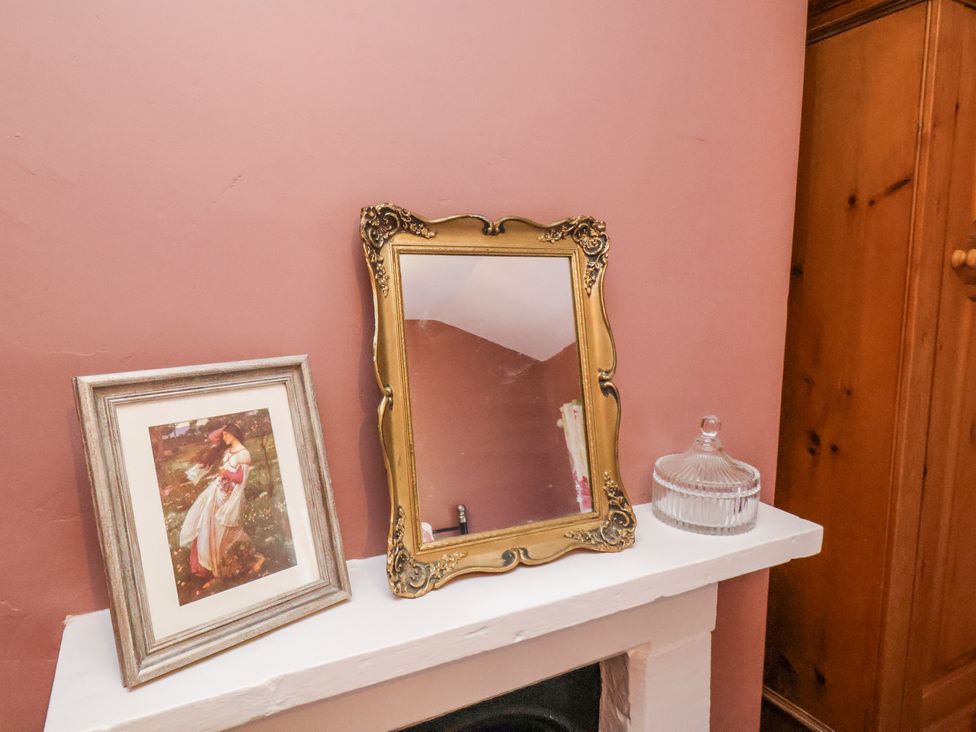 A mantelpiece with a framed picture a decorative mirror and a glass container at Whinstone Cottage Esk Valley near Grosmont