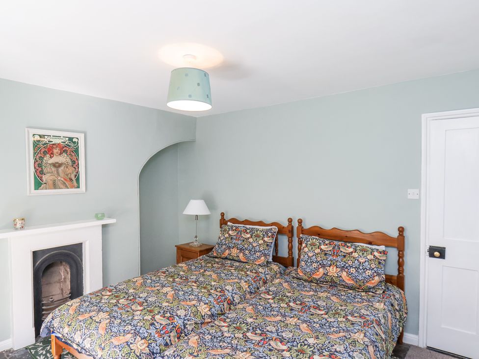 A bedroom with two single beds with patterned bedding a side table with lamp and a fireplace at Whinstone Cottage Esk Valley near Grosmont