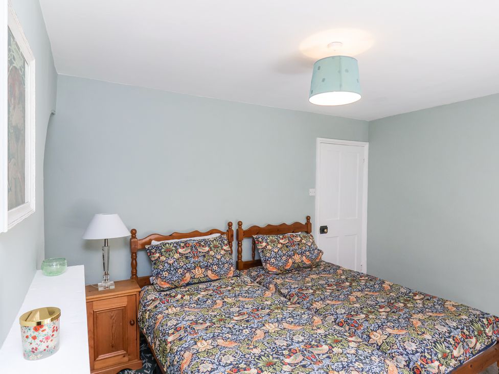 A bedroom with two single beds with patterned bedding a wooden nightstand with a lamp and a white door at Whinstone Cottage in Esk Valley near Grosmont