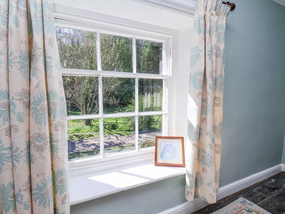 A window with floral curtains and a framed picture on the windowsill at Whinstone Cottage Esk Valley near Grosmont
