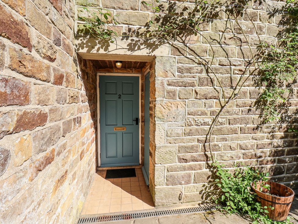 A blue door with the number 2 set in a stone wall with a tiled floor and a wooden planter nearby at Whinstone Cottage in Esk Valley near Grosmont