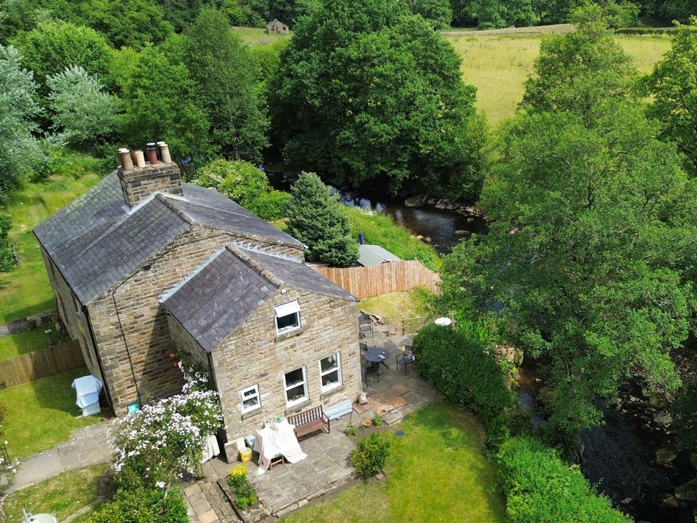 An outdoor view of a house with a stream beside it at Whinstone Cottage in Esk Valley near Grosmont