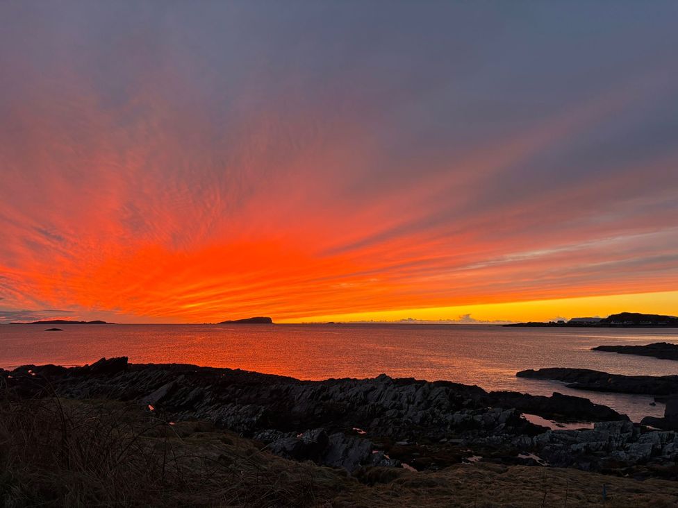 A sunset over the sea with rocky shore at Bathach Beag in Balvicar, Isle Of Seil