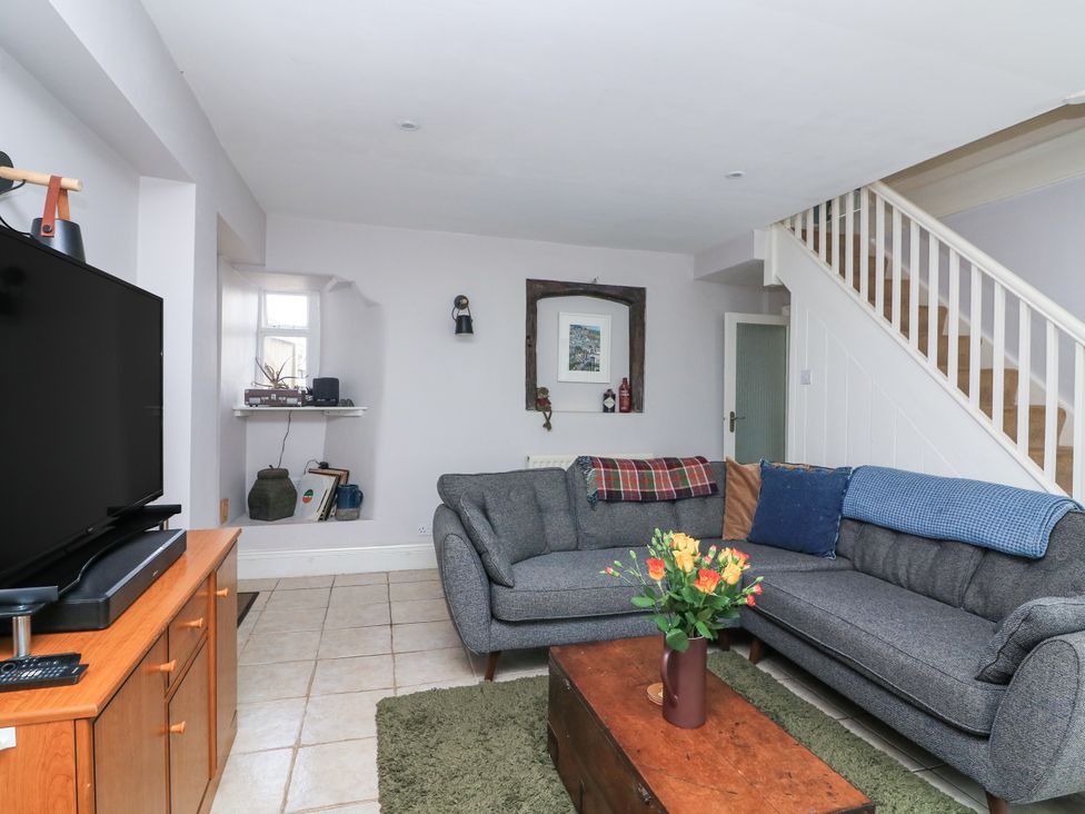 A living room with gray sectional sofa a wooden coffee table with flowers a television on a wooden stand and stairs at Joymead in Malborough