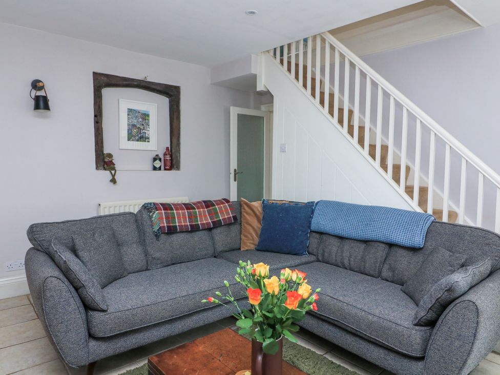 A living room with a grey sofa, throws and cushions, a wooden coffee table with flowers, stairs and a recessed wall shelf at Joymead in Malborough
