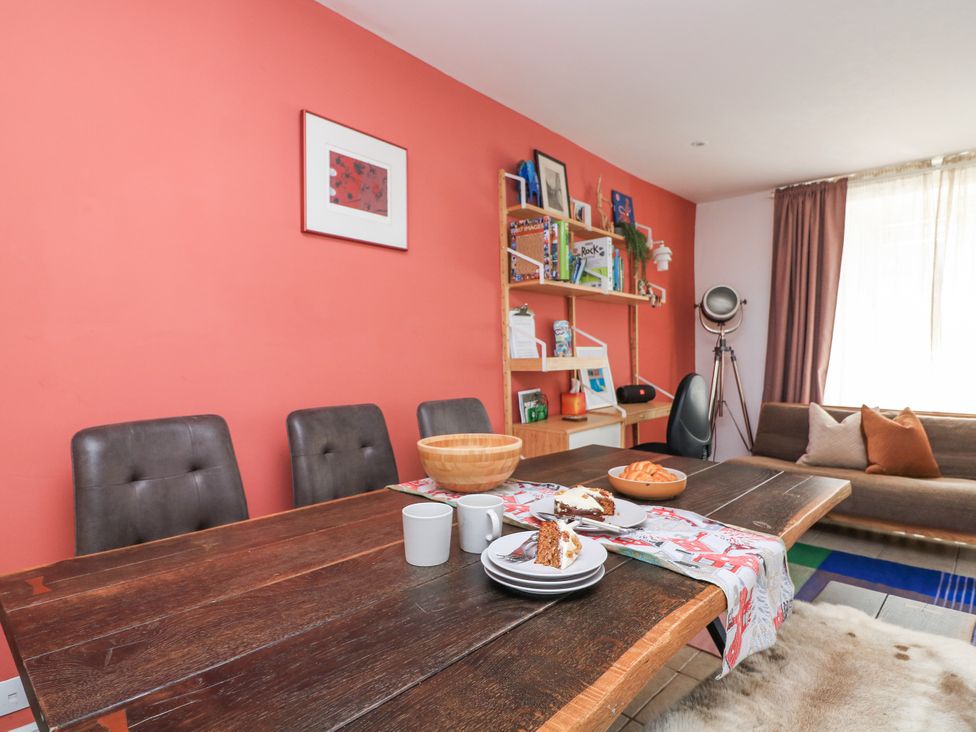 A dining room with a wooden table with food and mugs and chairs against a coral wall with bookshelves and a sofa at Joymead in Malborough