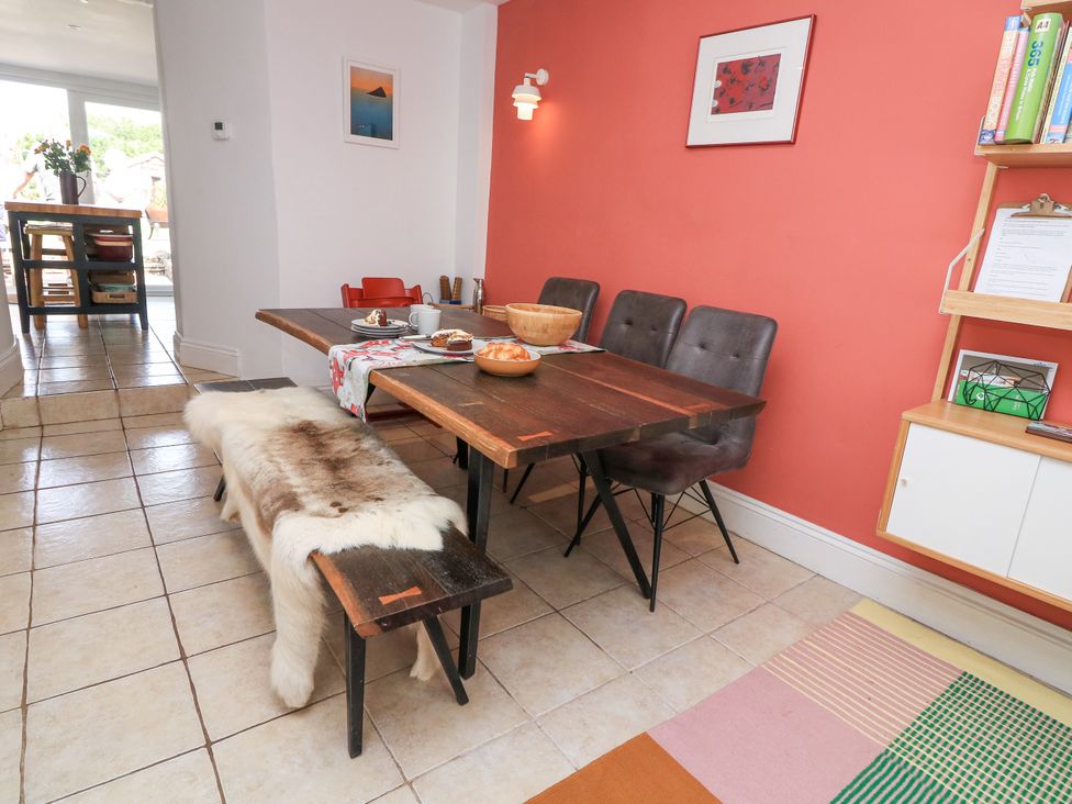 A dining area with a wooden table and chairs next to a coral colored wall with a framed picture and a wooden shelving unit at Joymead in Malborough