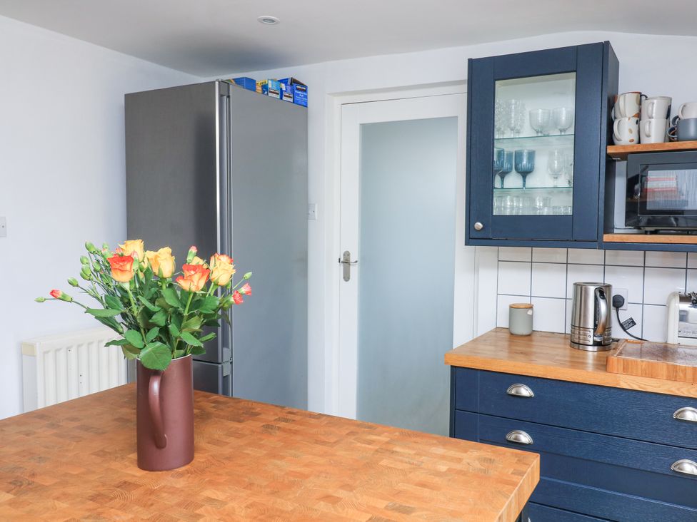 A kitchen with a wooden countertop a vase with flowers a silver refrigerator blue cabinets with glassware a kettle and a toaster at Joymead in Malborough