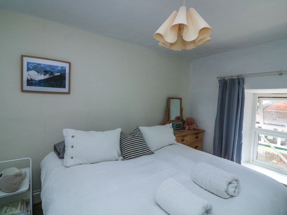 A bedroom with a large bed with white bedding pillows and rolled towels a wooden dresser and a window with blue curtains at Joymead in Malborough