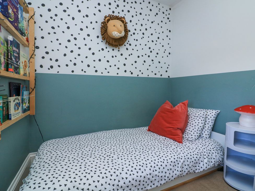 A bedroom with a single bed with patterned bedding and red pillows a round white side table with a mushroom lamp a wall mounted stuffed lion and a wooden bookshelf with books at Joymead in Malborough