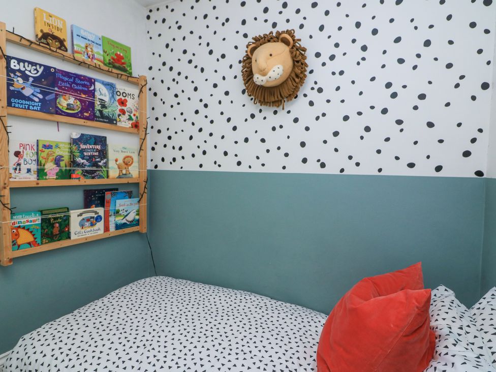 A children's bedroom with a bed with patterned bedding two red pillows a wall shelf with books and a lion head decoration on the wall at Joymead in Malborough