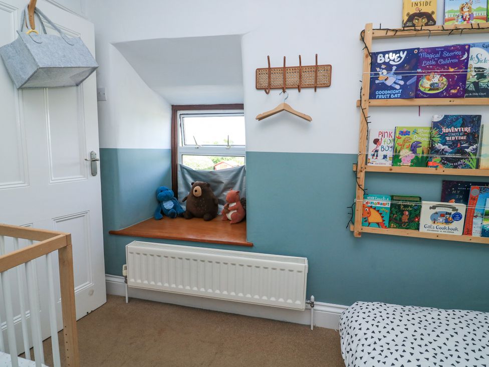 A children's room with a window seat holding stuffed animals a wall-mounted book shelf with children's books a white door with a gray hanging basket and a radiator below the window at Joymead in Malborough