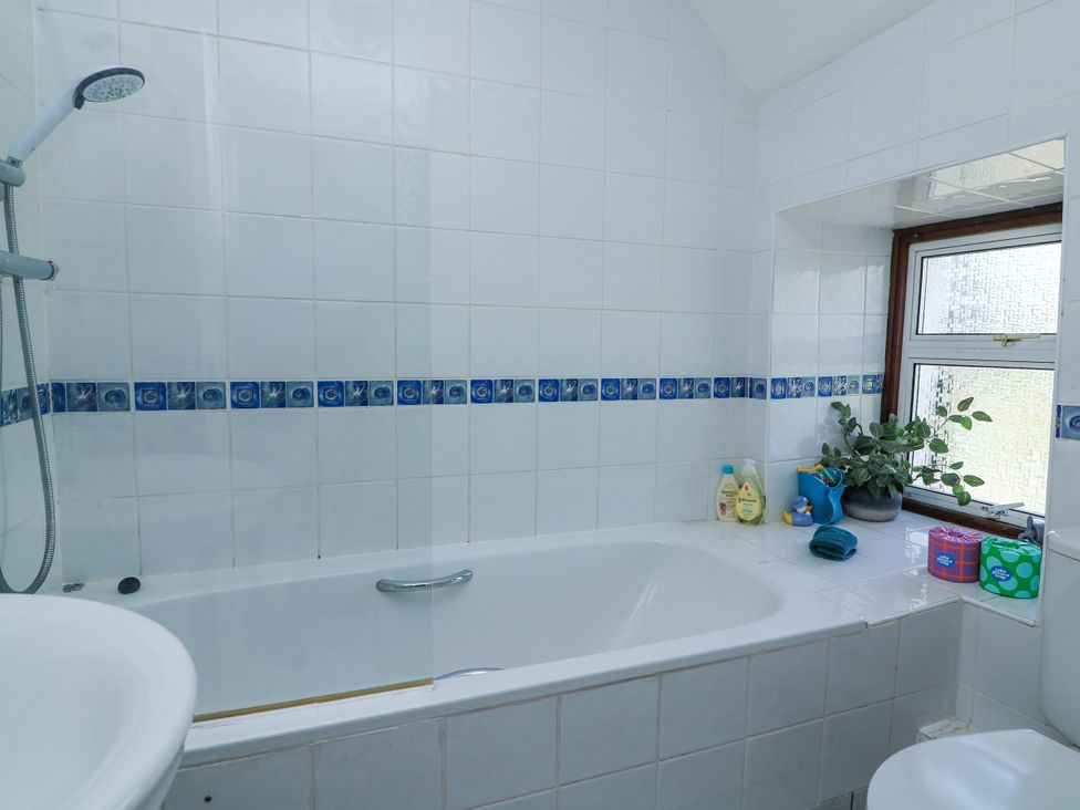 A bathroom with a bathtub shower combination a window with plants and toiletries at Joymead in Malborough
