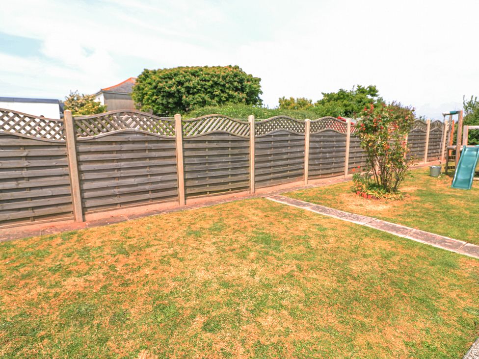 A backyard with a wooden lattice fence a patchy lawn a small bush and a children's slide at Joymead in Malborough
