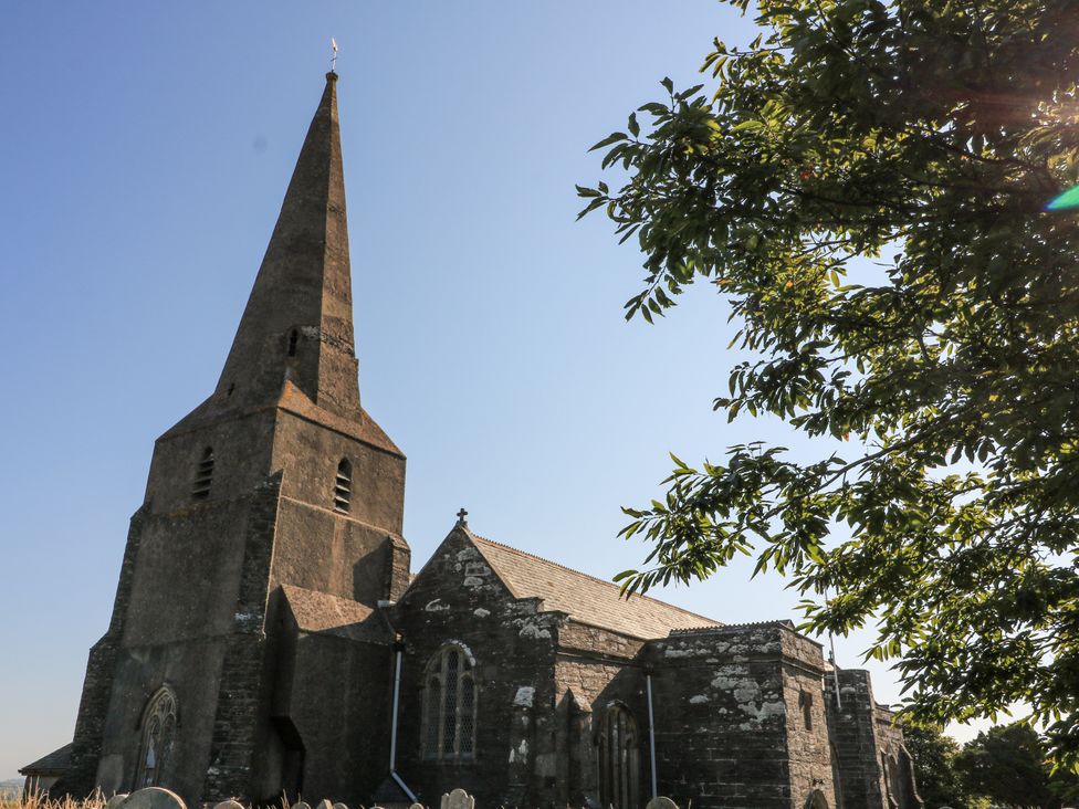 An old stone church with a tall spire and arched windows next to a tree with green leaves