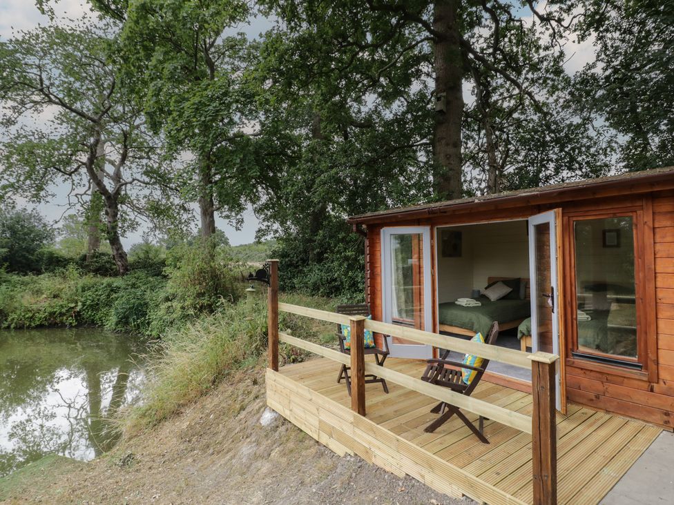 A wooden cabin with a deck near water at Carps Well Lodge Hatton near Shrewley