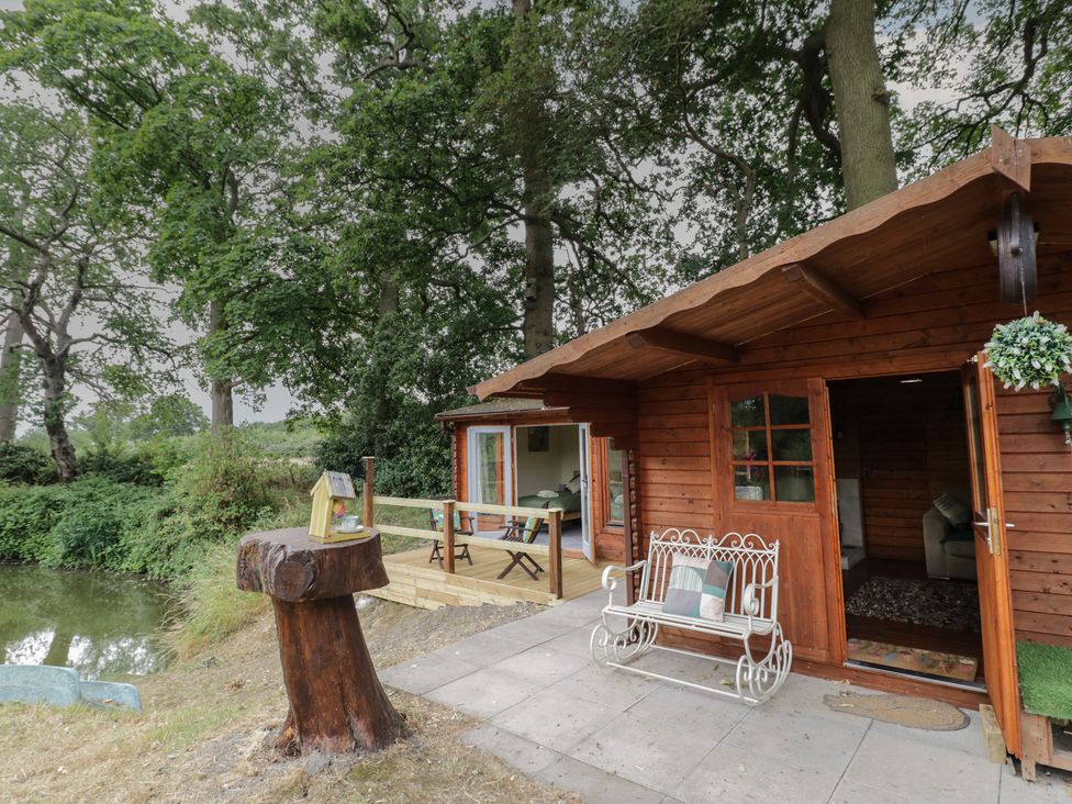 A cabin with wooden deck and bench at Carps Well Lodge Hatton near Shrewley