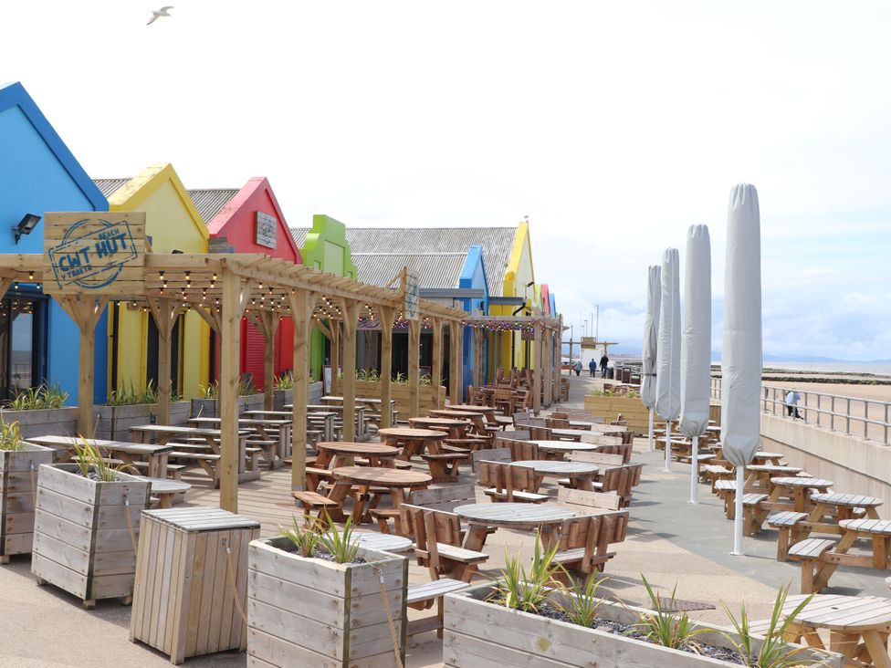 An outdoor dining area with wooden tables and colorful beach huts at 152 Central Park, Prestatyn