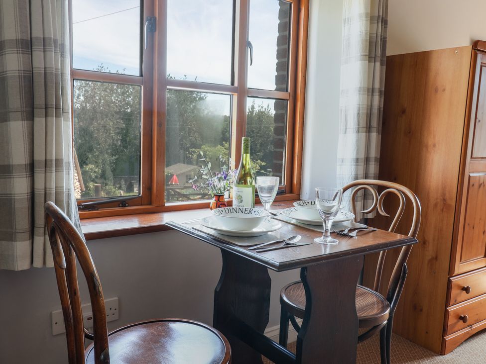 A small wooden dining table set for two by a window with two wooden chairs and a wooden wardrobe in a room at Megs Roost in Shute near Colyton