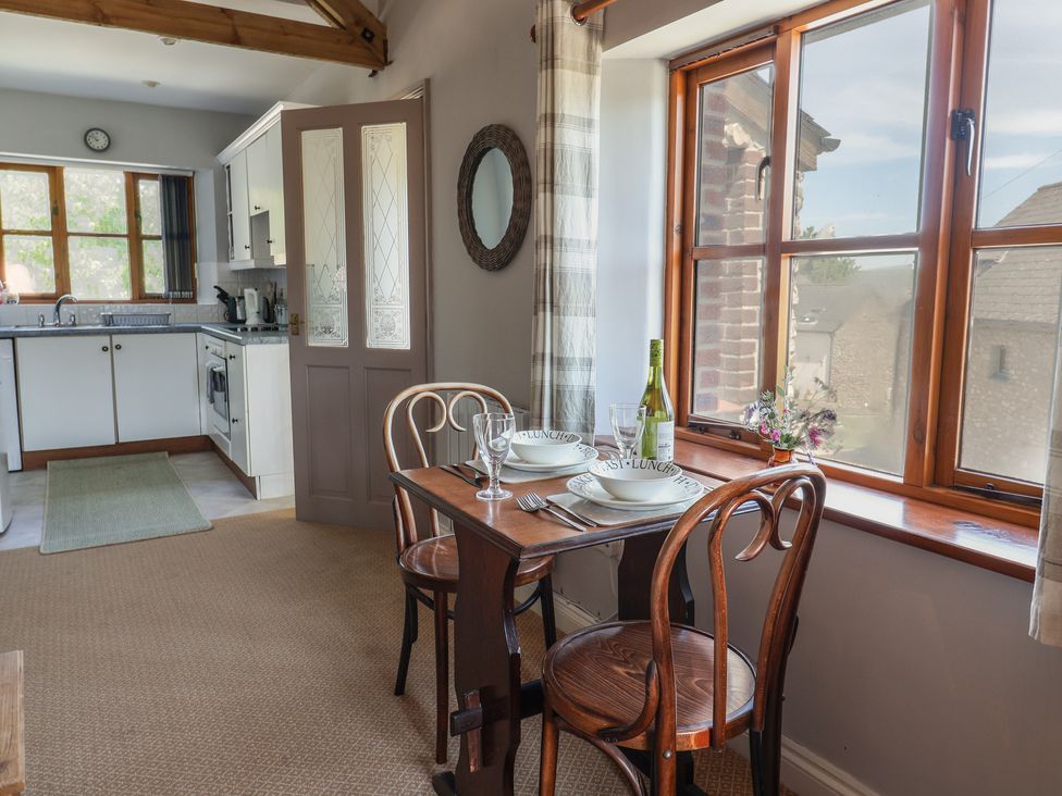 A kitchen and dining area with a wooden table set for two by a window at Megs Roost Shute near Colyton