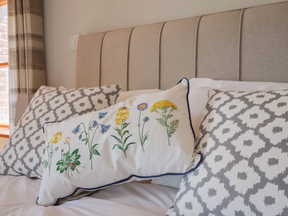 A bed with patterned pillows and a floral embroidered cushion at Megs Roost in Shute near Colyton