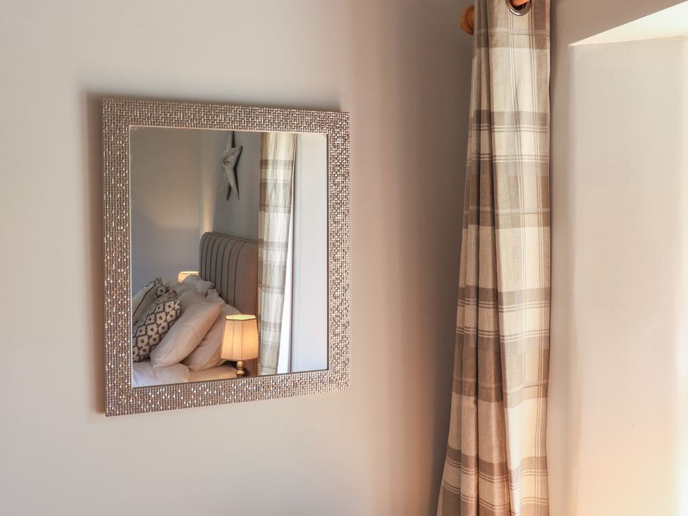 A mirror on a wall reflecting a bedroom with a bed a lamp and a star decoration with a checkered curtain nearby at Megs Roost Shute near Colyton