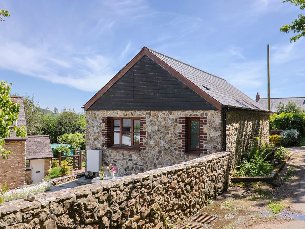 An exterior view of a stone cottage with two windows and a slate roof surrounded by a stone wall and garden at Megs Roost Shute near Colyton