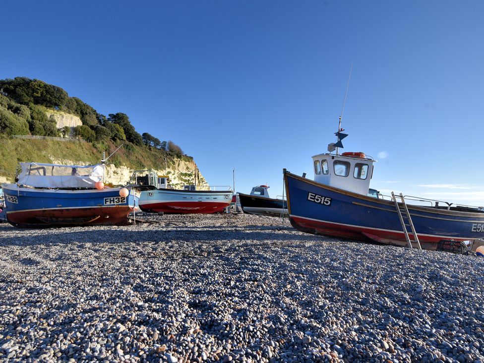 Fishing boats on a pebble beach with cliffs and trees in the background at Megs Roost in Shute near Colyton
